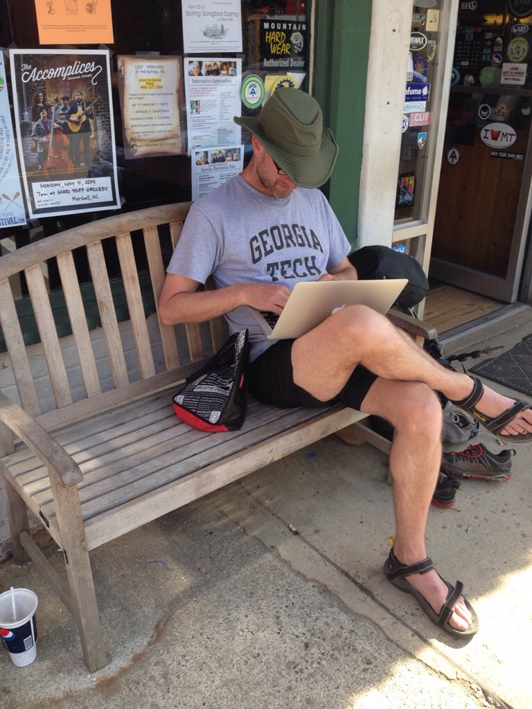 man in Georgia Tech shirt on laptop on bench